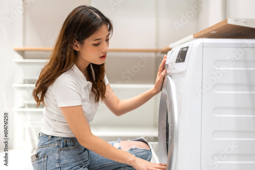 Maid asian woman having fun doing household chores doing laundry dirty clothes into the washing machine in laundry room, housewife, housework, girl cleanup clothes at home