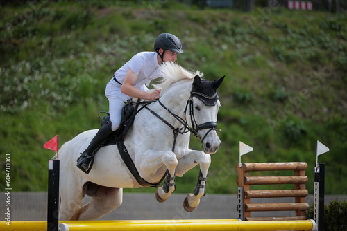 Show jumper with a white horse jumping over an obstacle, close-up from the right front..
