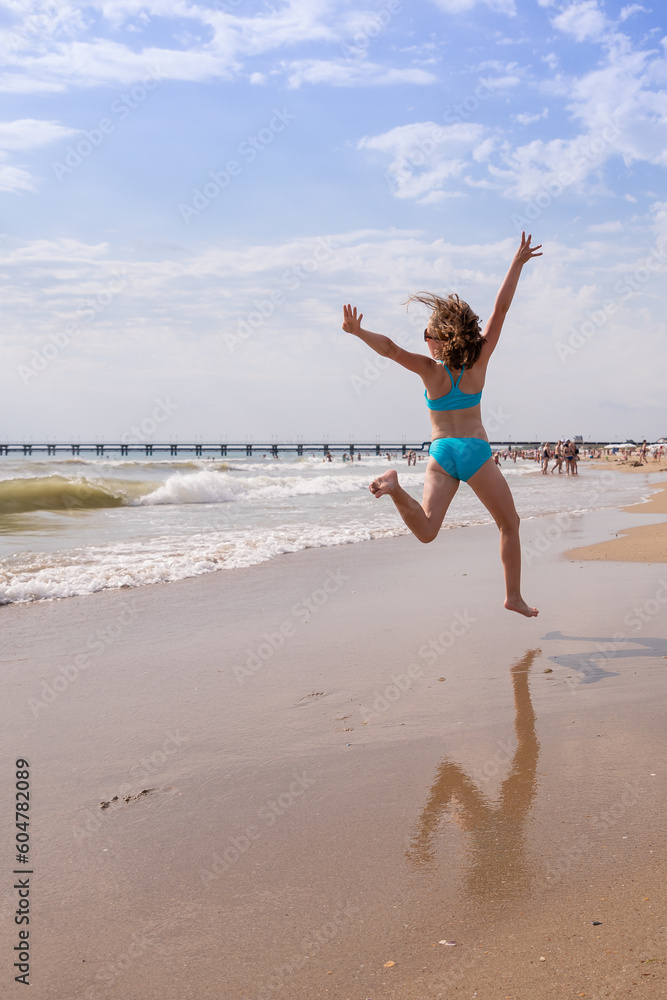 girl has a swimsuit, having fun alone on the sand in summer by the sea. female child dancing by the water while on holiday or vacation.happy and smiling girl performs gymnastic, dance exercises girl has a swimsuit, having fun alone on the sand in summer by the sea. female child dancing by the water while on holiday or vacation.happy and smiling girl performs gymnastic, dance exercises
