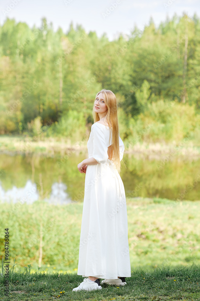 Full length portrait of young woman in long dress on river bank