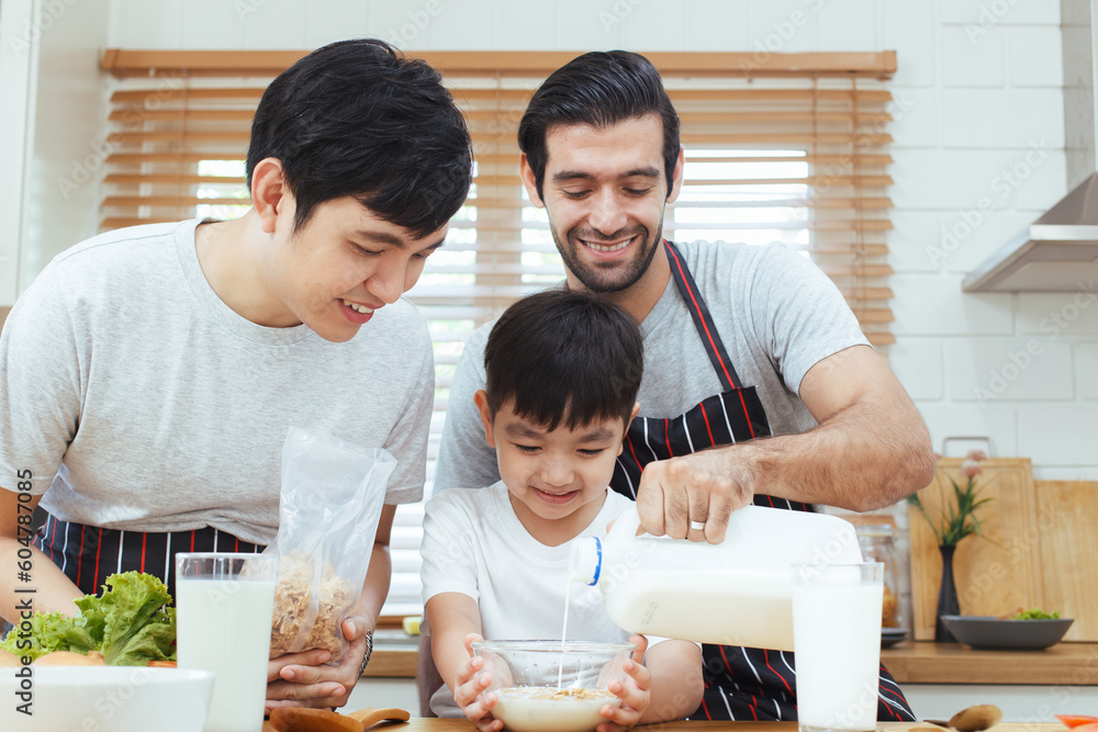 Happy cheerful gay couple with their adopted little son enjoy making a corn flakes with fresh milk for breakfast in the kitchen together. Happy LGBTQ+ family with adopted child concept. Happy cheerful gay couple with their adopted little son enjoy making a corn flakes with fresh milk for breakfast in the kitchen together. Happy LGBTQ+ family with adopted child concept.