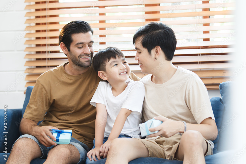 Lovely little boy gives fathers a present in the father's day festival, happy Asian and Caucasian gay couple with foster son. A diversity in gender - LGBTQ and ethnicity concept. Lovely little boy gives fathers a present in the father's day festival, happy Asian and Caucasian gay couple with foster son. A diversity in gender - LGBTQ and ethnicity concept.