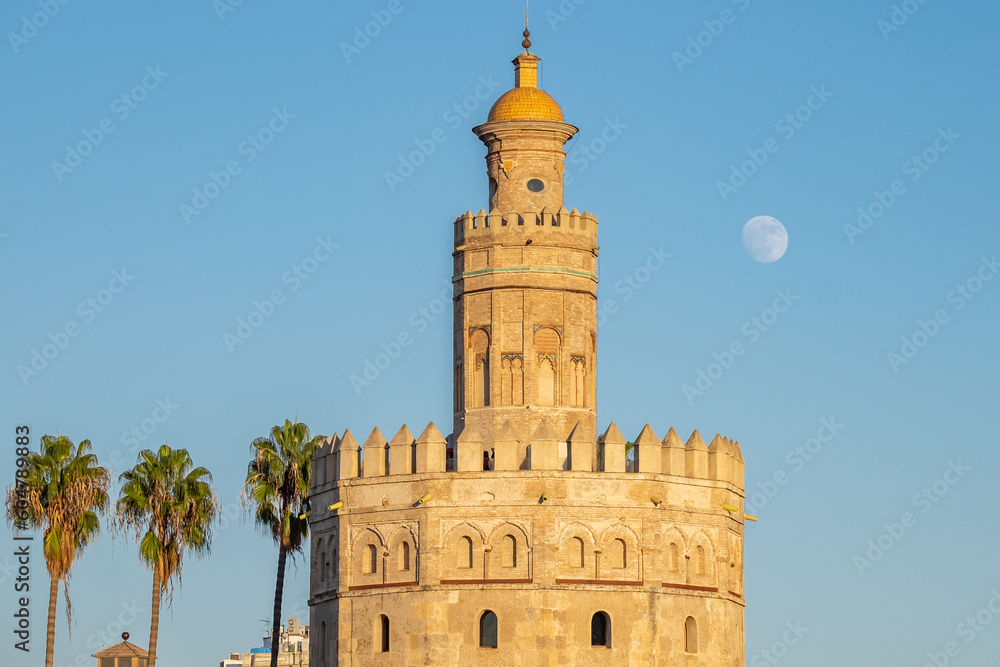 View of seville's Torre del Oro with a blue sky and full moon in a sunny day.
