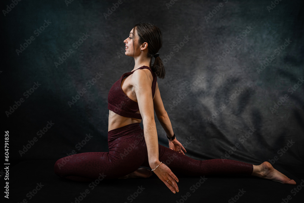 Fitness woman doing yoga or stretching exercises on mat against dark black background