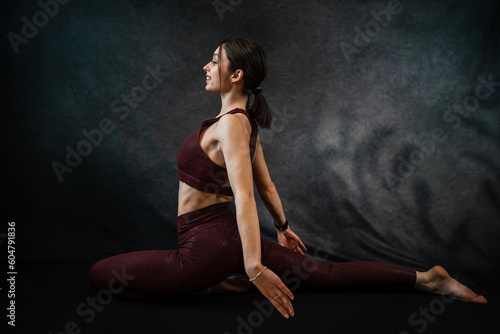Fitness woman doing yoga or stretching exercises on mat against dark black background