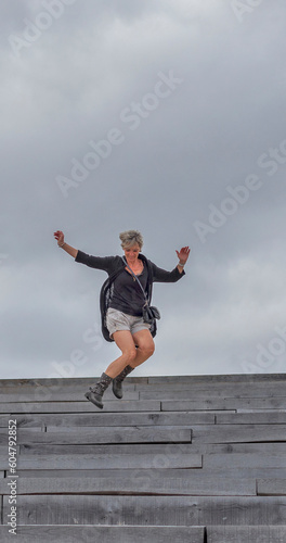 A woman in her fifties jumps smiling on a staircase.