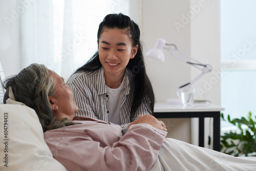 Smiling young woman taking to her sick senior mother staying in bed