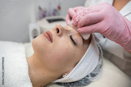 cosmetologist masseur doing faacial anti-agging procedure with gouache scraper for her client