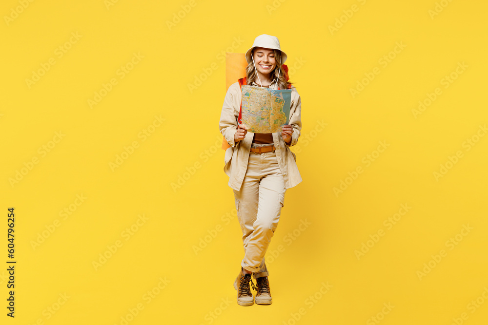 Full body cheerful happy young woman carry bag with stuff mat reading map isolated on plain yellow background. Tourist leads active lifestyle walk on spare time. Hiking trek rest travel trip concept. Full body cheerful happy young woman carry bag with stuff mat reading map isolated on plain yellow background. Tourist leads active lifestyle walk on spare time. Hiking trek rest travel trip concept.