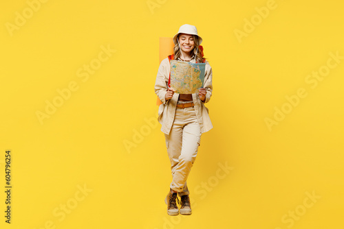 Full body cheerful happy young woman carry bag with stuff mat reading map isolated on plain yellow background. Tourist leads active lifestyle walk on spare time. Hiking trek rest travel trip concept.