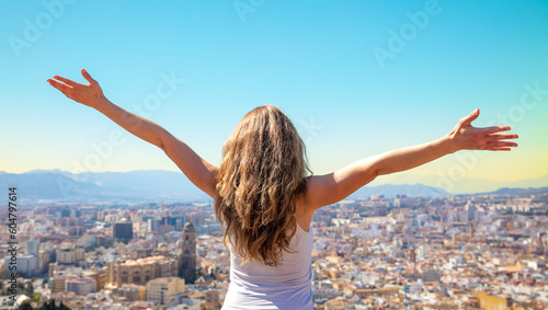 Happy free woman with arms up admiring skyling of Malaga city- City skyline with arms outstretched raised in the sky- success, travel, active life concept