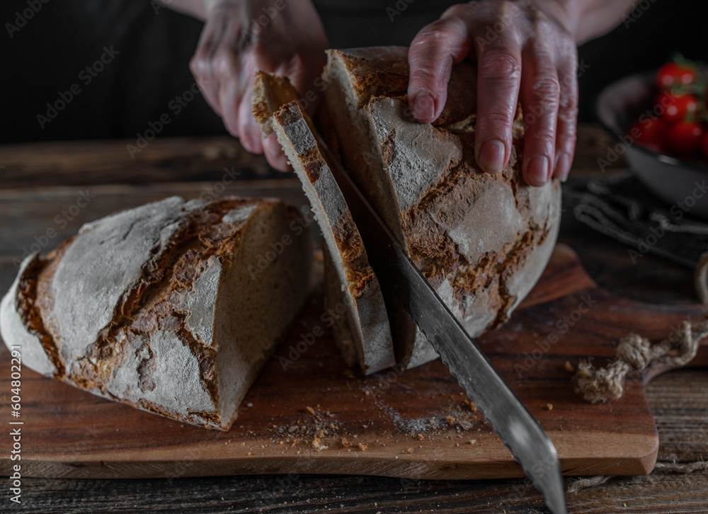 Slicing sourdough bread on a rustic and wooden cutting board. Slicing sourdough bread on a rustic and wooden cutting board.