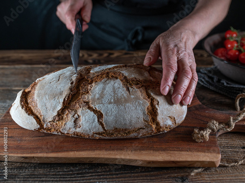 Cutting rustic loaf of sourdough bread by womans hand with a bread knife