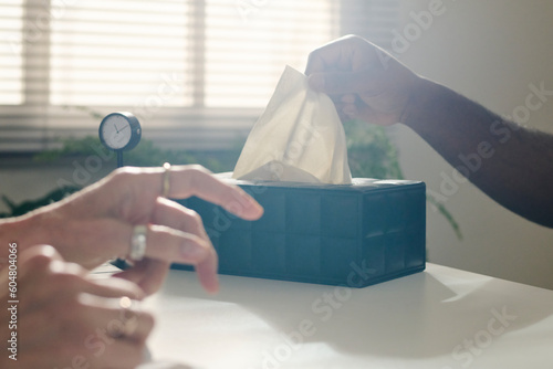 Hand of patient pulling paper napkin from box at desk in office photo