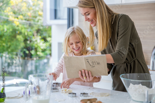 Happy woman reading recipe book by daughter preparing food in kitchen at home photo