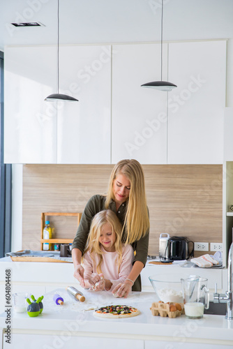 Girl learning to knead dough with mother in kitchen at home