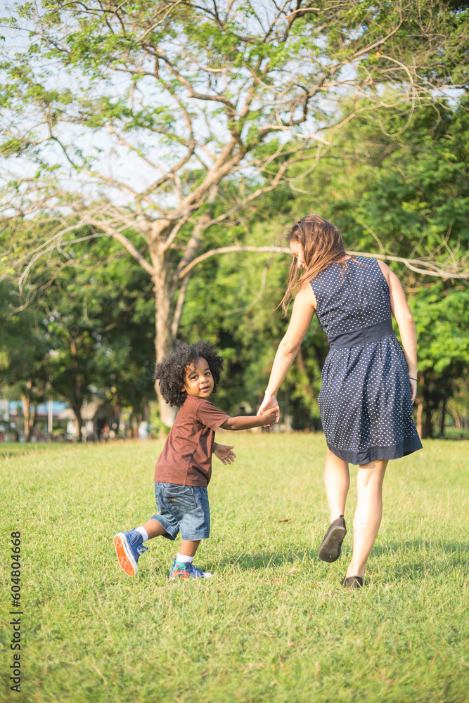 Mother and son holding hands and walking on grass at park Mother and son holding hands and walking on grass at park