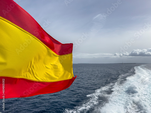 Spain, Balearic Islands, Formentera, Wake left by moving boat with Spanish flag fluttering in foreground photo