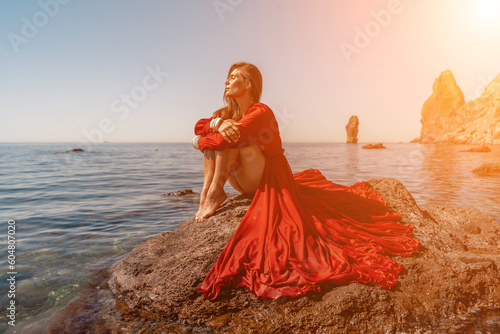 woman sea red dress. Beautiful sensual woman in a flying red dress and long hair, sitting on a rock above the beautiful sea in a large bay.