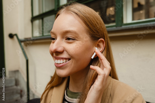 Portrait of smiling woman listening music with earphones while standing outdoors