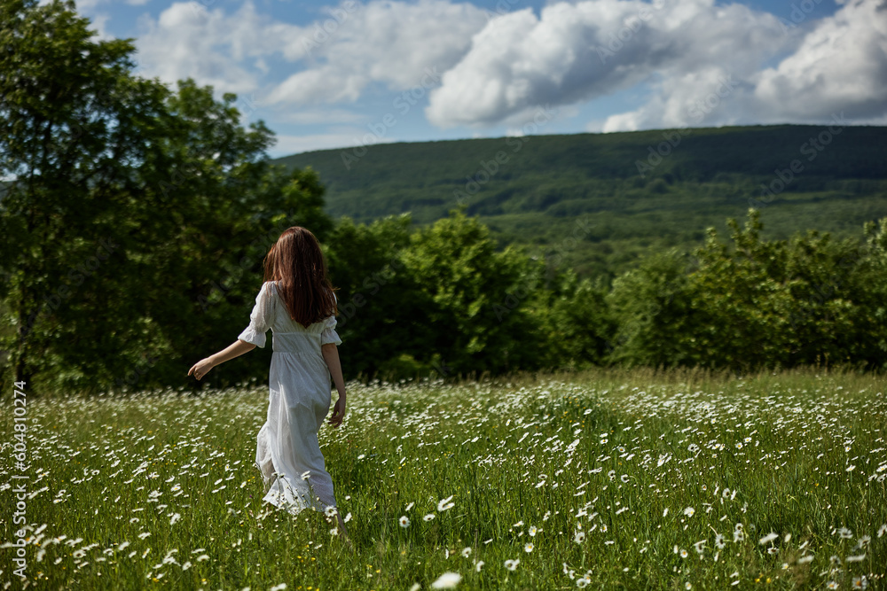 a free woman in a light dress runs through a field of daisies with her back to the camera