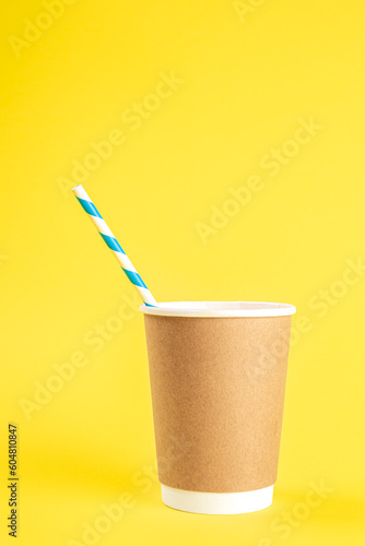 Disposable cup with a straw on a yellow background isolated.