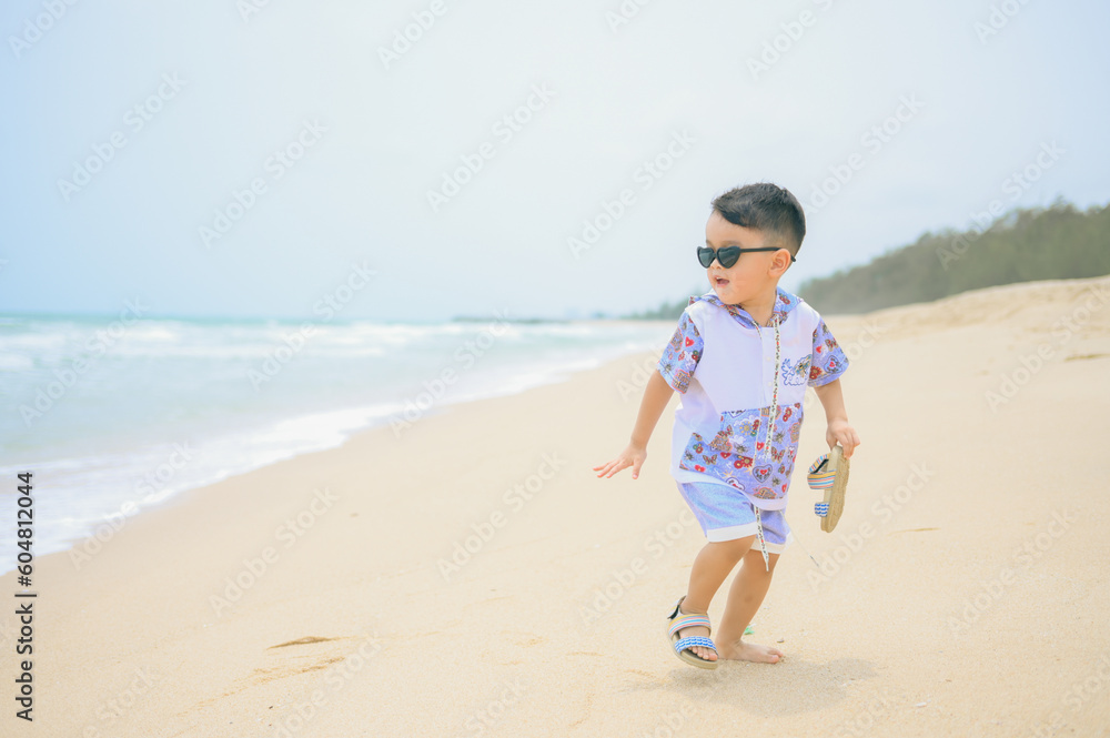 Asian boy wearing sunglasses is playing on a sandy beach near the sea. Asian boy wearing sunglasses is playing on a sandy beach near the sea.