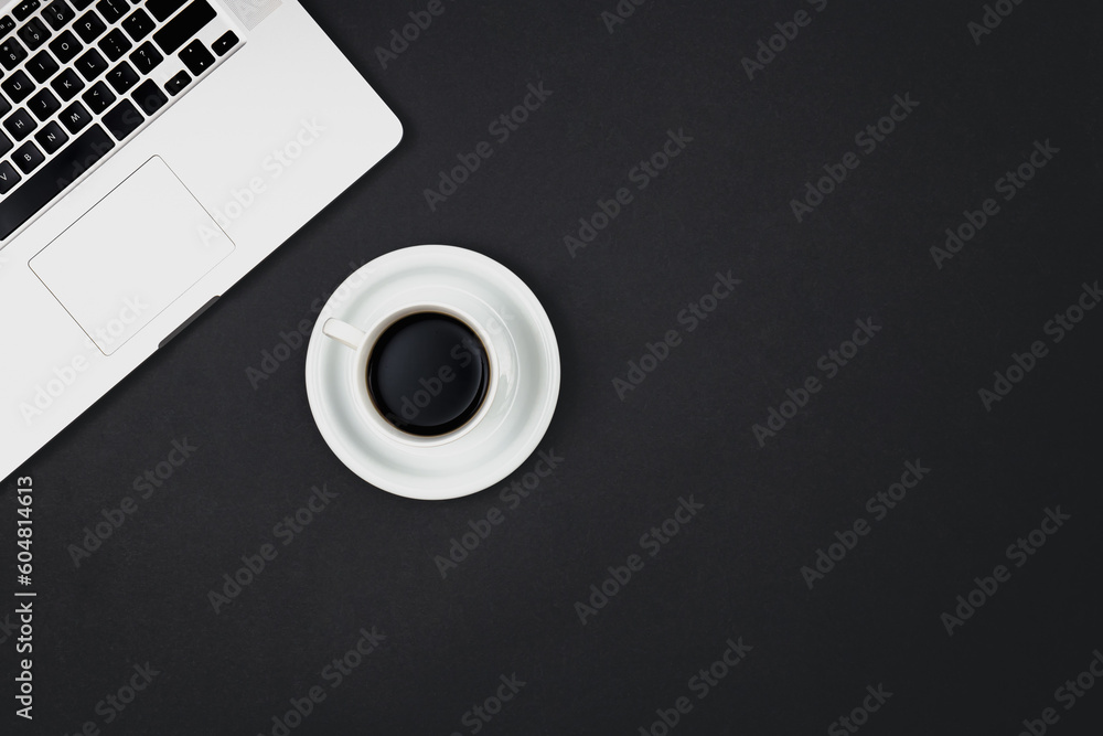 Laptop and coffee cup on black background, top view.