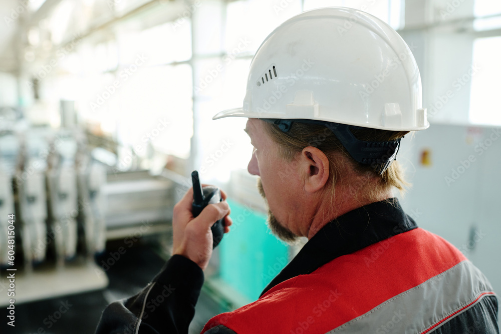 Rear view of worker in helmet using radio set in his work in plant Rear view of worker in helmet using radio set in his work in plant