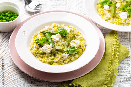 Risotto with green pea and asparagus with robiola cheese on a pink plate. Homemade spring rice food on a white table.