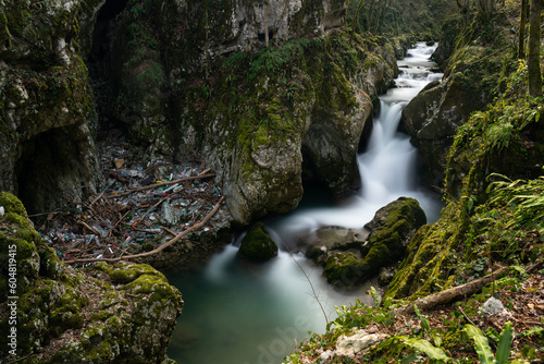 Waterfall with mossy rocks in mountain canyon and plastic waste problem, Svrakava river near Banja Luka