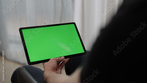 Man sitting indoors on a chair with tablet pc with green screen