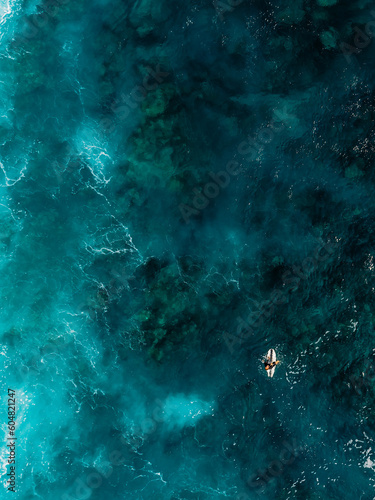 Aerial view of deep blue ocean with surfer in clear sea water and reef under water.