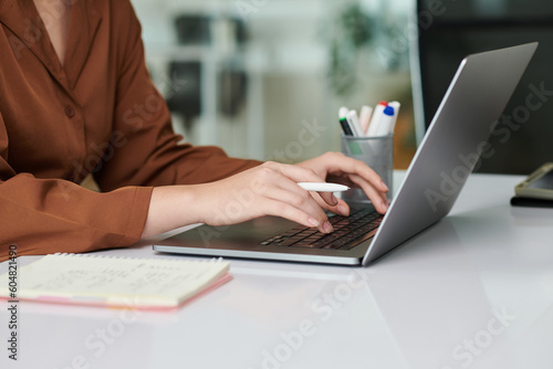 Hands of female entrepreneur working on laptop, checking e-mails and writing in planner