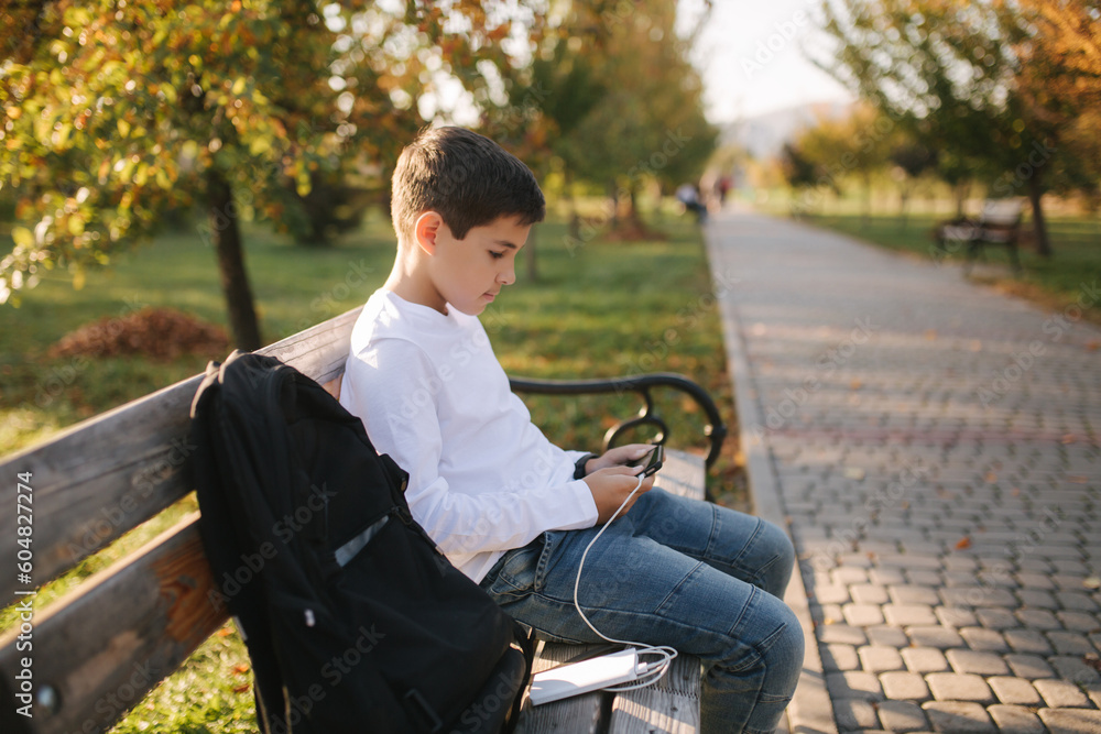 Teenage boy in white shirt use powerbank for charging his smartphone otside. Low battery on smartphone Teenage boy in white shirt use powerbank for charging his smartphone otside. Low battery on smartphone