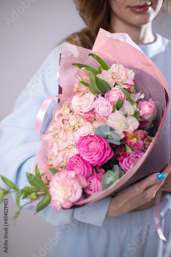 A woman is holding a bouquet of flowers. The florist creates a pink beautiful bouquet of mixed flowers. Peony roses. Flower shop. Fresh bouquet. Master class and floristry courses. Flower delivery.