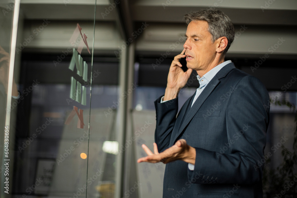 Portrait of successful businessman in office. Man writing on the glass board in office. Businessman talking to the phone.. Portrait of successful businessman in office. Man writing on the glass board in office. Businessman talking to the phone..