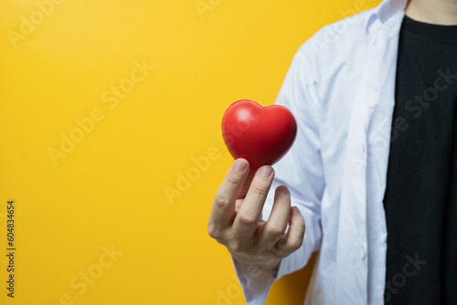 Doctor hand holding red heart on yellow background Cardiology, medicine, donation and healthcare concept