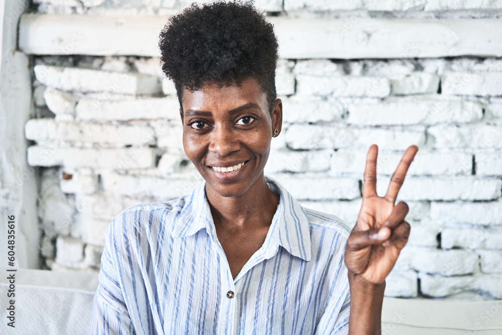 Obraz premium A miggle-aged african woman sitting on her sofa showing number two with fingers.