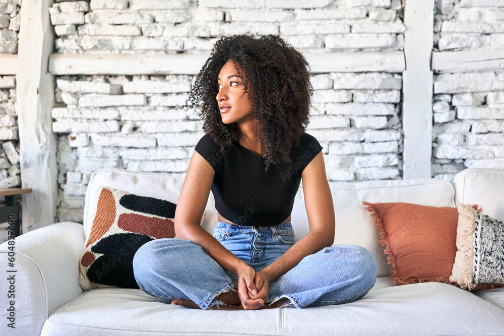 Afro-haired woman relaxes on sofa, basking in soft morning light at home. Afro-haired woman relaxes on sofa, basking in soft morning light at home.