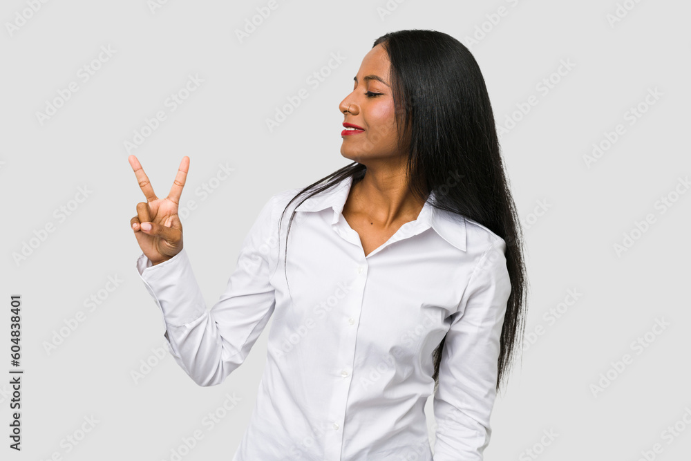 Young Indian woman cut out isolated on white background joyful and carefree showing a peace symbol with fingers. Young Indian woman cut out isolated on white background joyful and carefree showing a peace symbol with fingers.