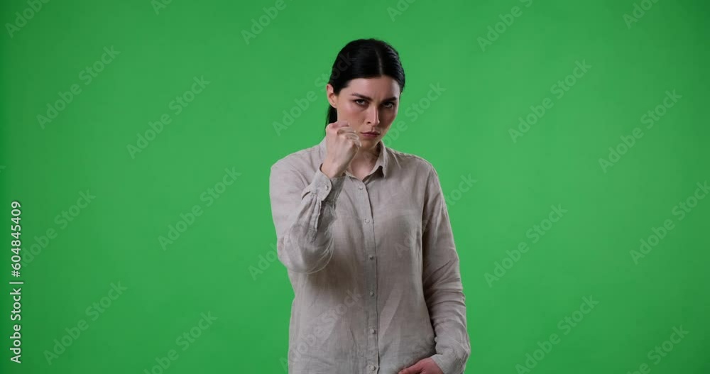 Angry Caucasian woman standing on a green screen background. She shows the shush gesture with her finger near her lips, followed by a threatening fist gesture. Angry Caucasian woman standing on a green screen background. She shows the shush gesture with her finger near her lips, followed by a threatening fist gesture.
