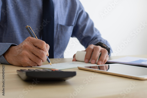 Business man hand writing and signing cheque book with laptop computer on the wooden table at modern home office. 