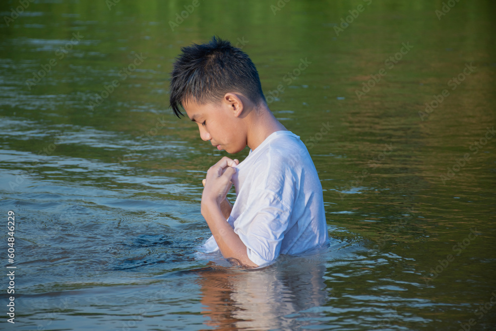 Fototapeta premium Asian boy in white t-shirt is spending his freetimes by diving, swimming, throwing rocks and catching fish in the river happily, hobby and happiness of children concept, in motion.
