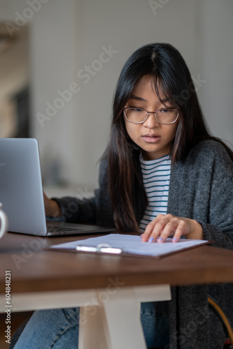 Long-haired young asian girl in eyeglasses looking serious and involved © zinkevych