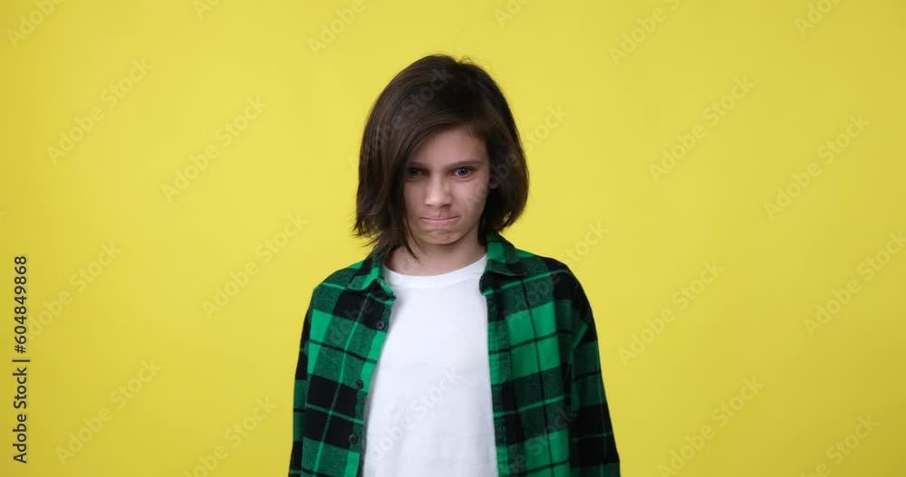 Young caucasian boy wearing a plaid shirt stands on a yellow background, angrily gesturing and expressing his emotions with intense facial expressions. Young caucasian boy wearing a plaid shirt stands on a yellow background, angrily gesturing and expressing his emotions with intense facial expressions.