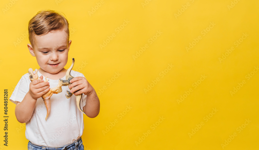 Cute laughing little boy on a yellow background with a dinosaur toy in his hands. Copy space. Cute laughing little boy on a yellow background with a dinosaur toy in his hands. Copy space.