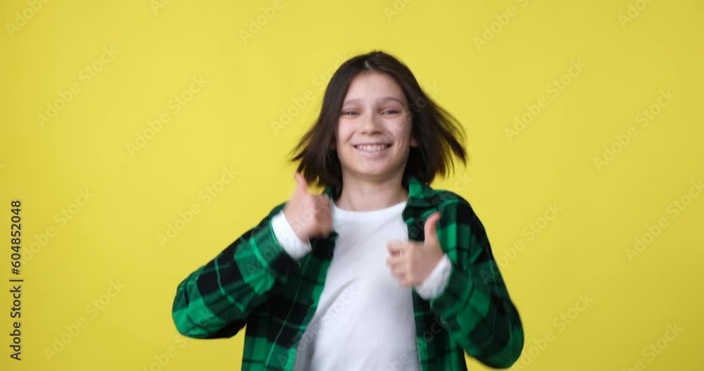 Boy stands on a yellow background wearing a plaid shirt. He looks into the camera, smiles, and gives a thumbs up gesture, indicating approval or liking something. Boy stands on a yellow background wearing a plaid shirt. He looks into the camera, smiles, and gives a thumbs up gesture, indicating approval or liking something.