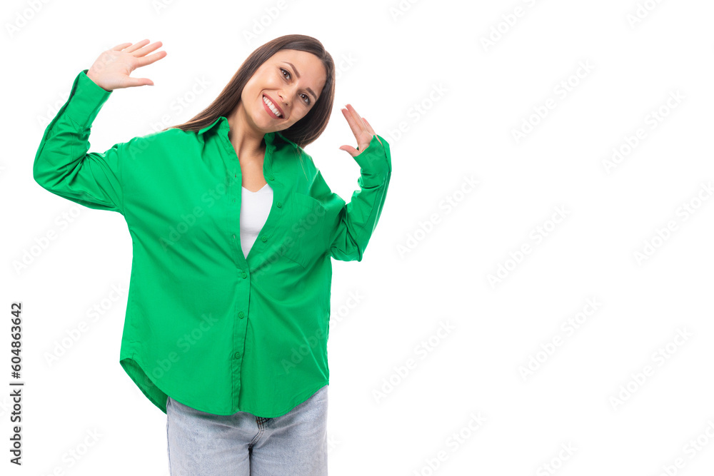 Fototapeta premium bright cheerful young brown-haired female model with brown eyes in a green shirt posing on a white background with copy space