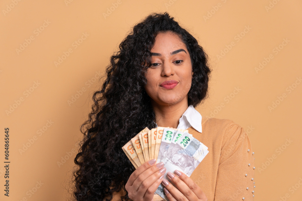 serious-black-woman-looking-at-brazilian-money-cash-in-beige-background